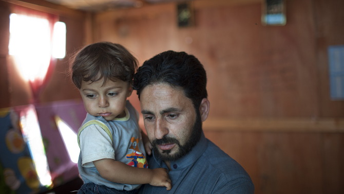 Ahmad holds his son Mouath in their makeshift home in the Ketermaya refugee camp; Photo © Dominic Chavez
