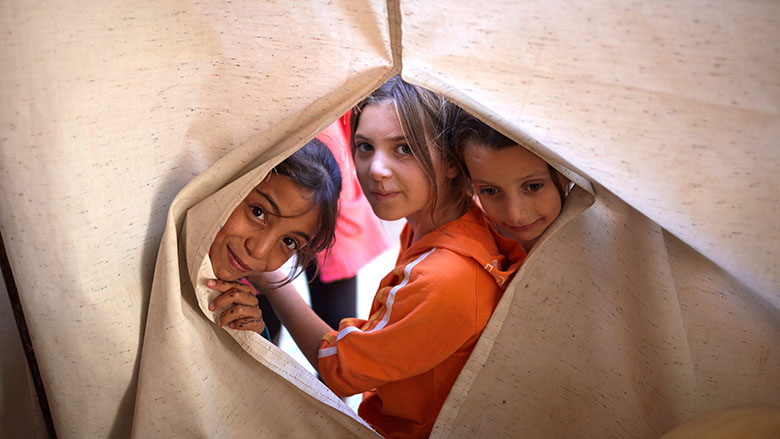 Syrian refugee children look through a sheet at the Nour Beach House in Chekka, Lebanon - © UNHCR/Shawn Baldwin