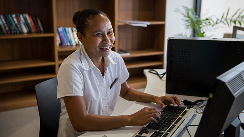 A woman that is employed at a hotel in Papua New Guinea smiles while sitting at her computer