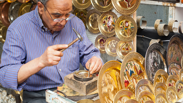 A craftsman punches out a pattern on a decorative brass plate at the souq market in Tunis, Tunisia.