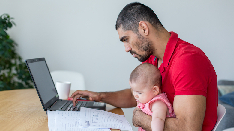 Business man works at home on his laptop with his daughter on his lap.