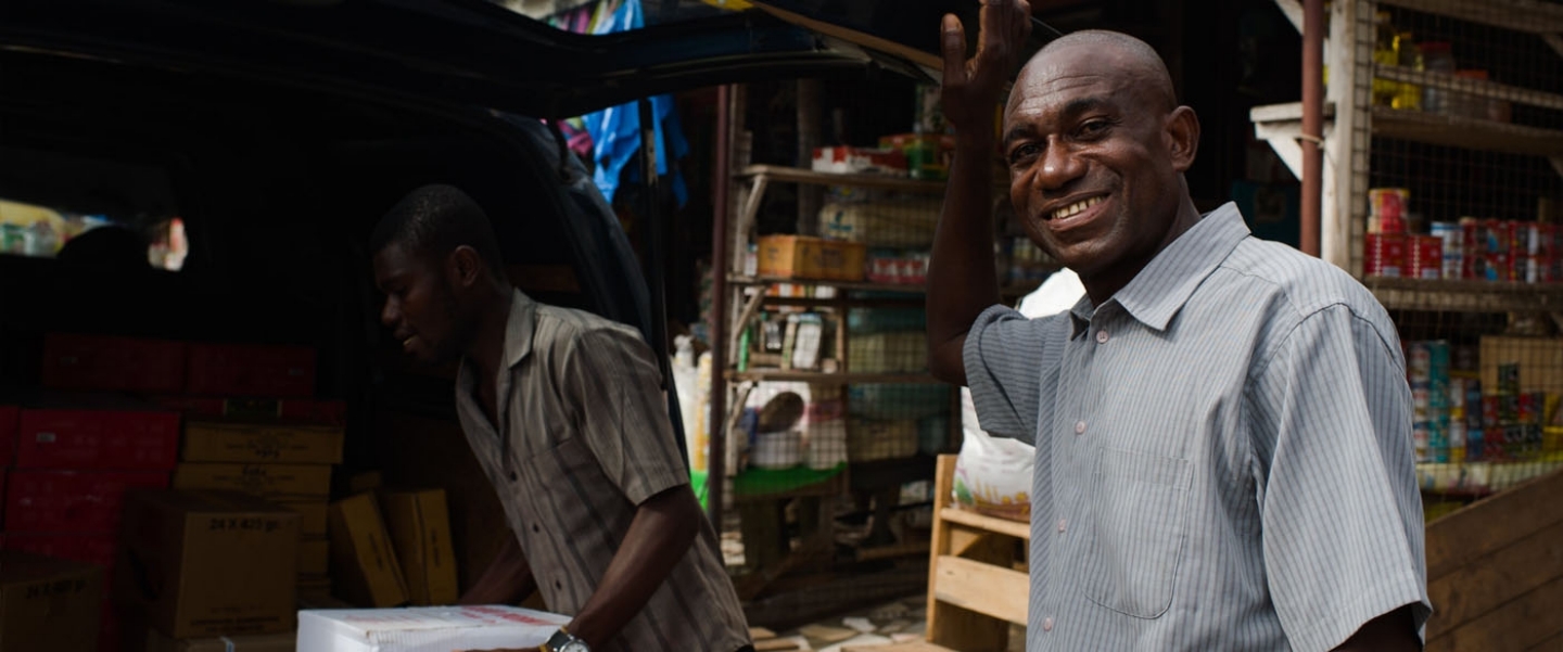 A man poses for a picture as his van is loaded with goods