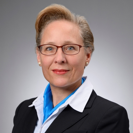 Female with short blonde hair wearing eye glasses, black suit, white blouse and blue neck scarf