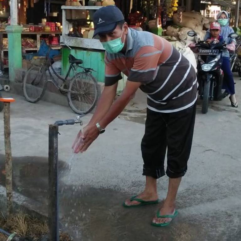 Man wearing face mask washing his hands at a public tap in Indonesia.
