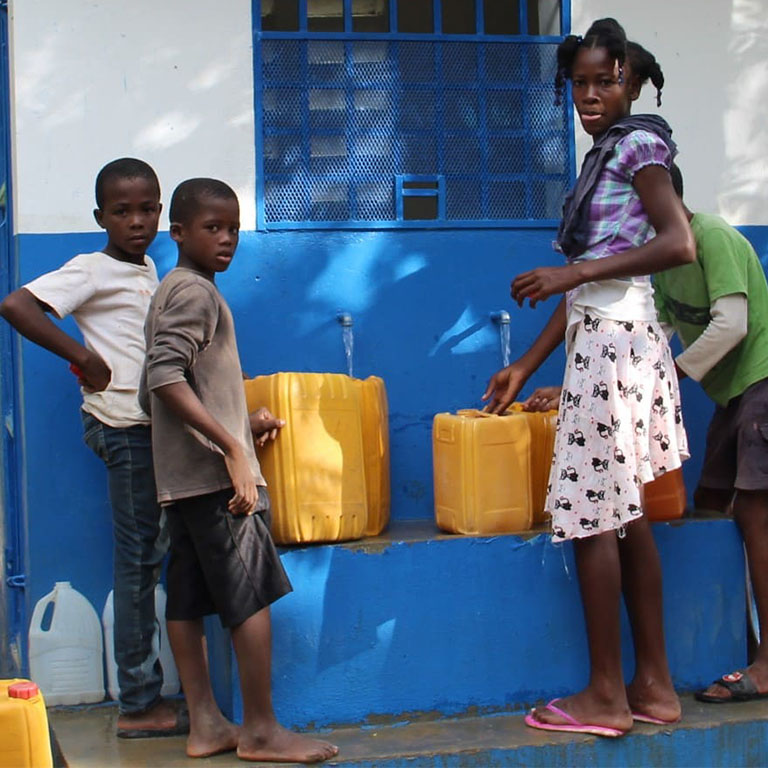 Boys and girls from Roche-à-Bateau, in Haiti, collect water from a community tap
