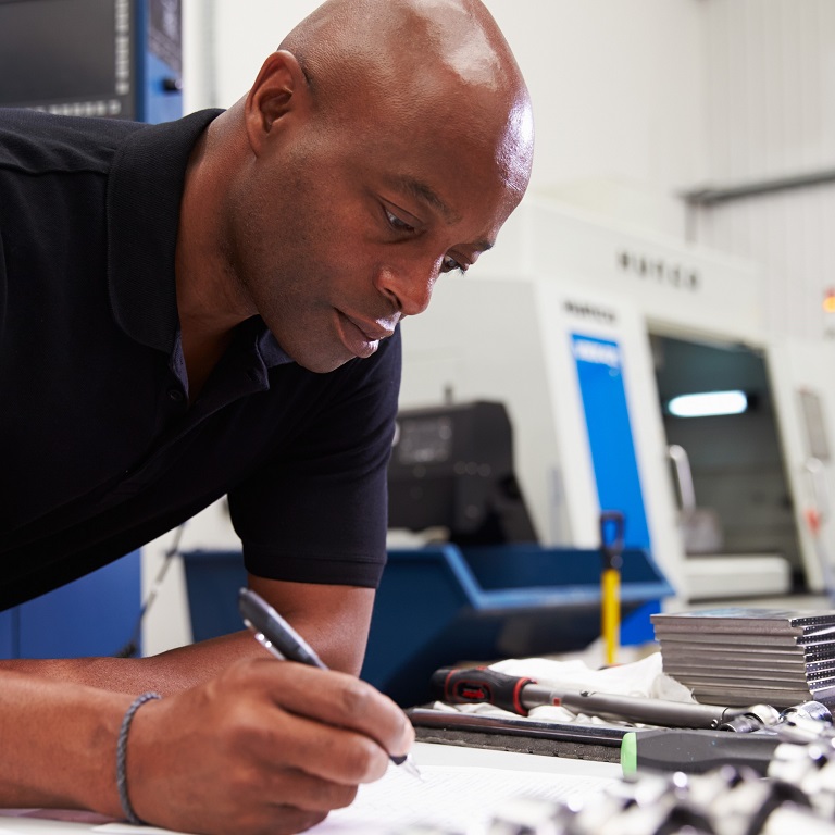 Engineer Planning Project With CNC Machinery In Background
