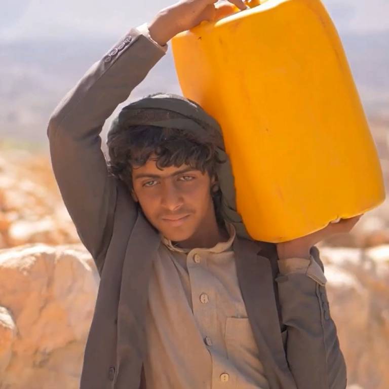 A young man carrying a large container of water in Yemen.