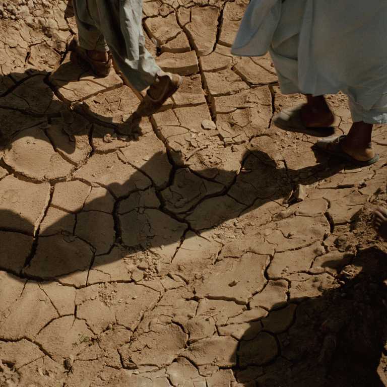 Shadows of men walking over cracked, dry land. Photo: Stephen_Dupont