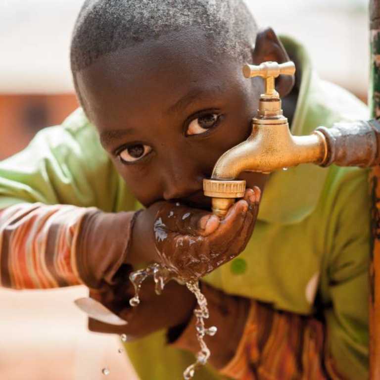 A boy drinks water from a tap.