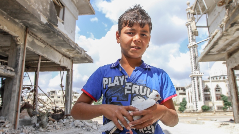 Boy near the destroyed house holding a white dove. 