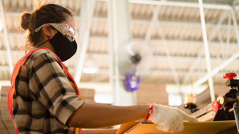 A female factory worker wears a mask while cutting wood