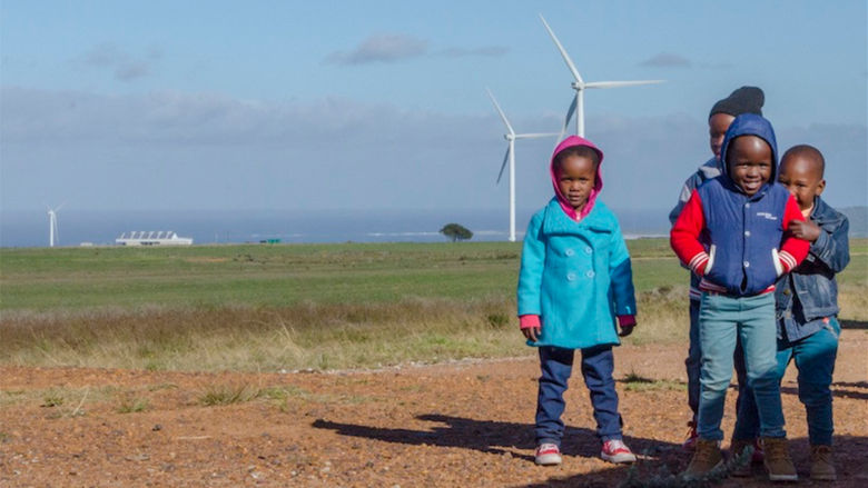 Children stand together with a wind farm in the distance