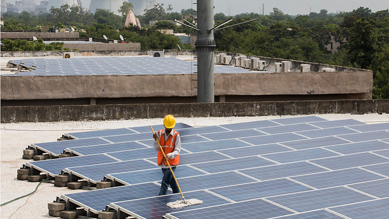 worker cleans solar panels on the rooftop of a building in Gandhinagar, India