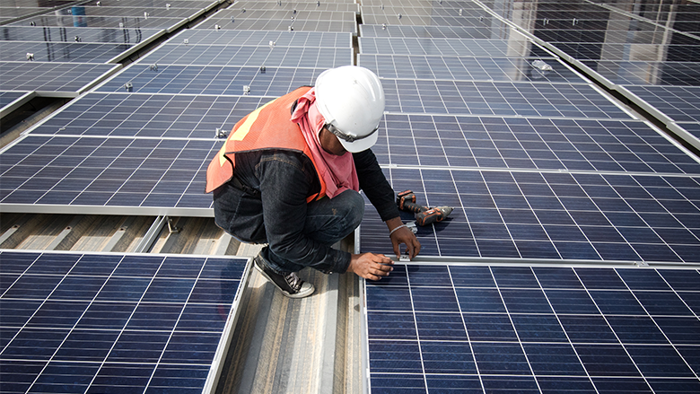 A technician installs solar panels on a factory roof in Bangkok, Thailand