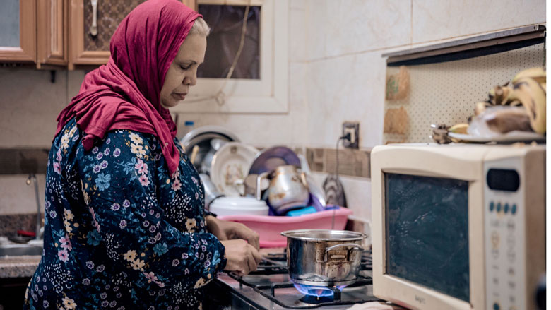 An Egyptian lady cooking food in the kitchen on a natural gas stove. 