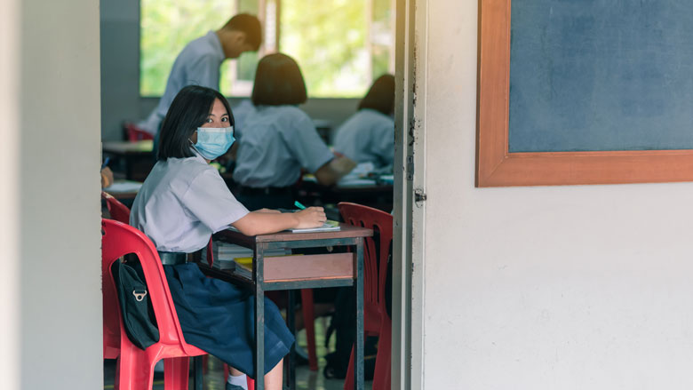 A high school student wearing a mask is sitting in a classroom during the COVID-19 pandemic. Photo: © Shutterstock