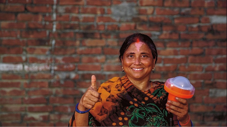 Indian woman smiling at the camera with her thumbs up, holding a solar lamp. 