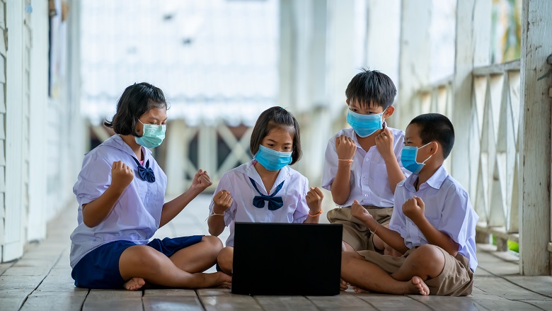 Group of students wearing protective mask to Protect Against Covid-19 use laptop to have online class happily at Thailand school classroom. Photo credit: Getty Images