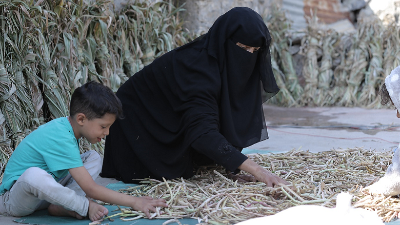 Woman drying out beans inside her house yard with a child by her side