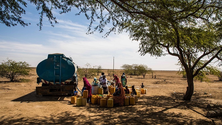 A group of women collecting water under a tree in an arid field, in the region of Saint Louis, Senegal.