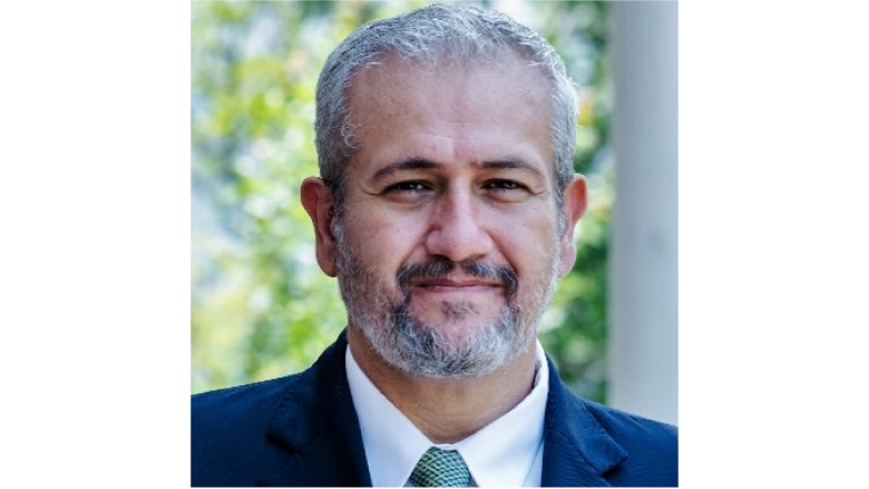 Male with grey hair and beard wearing blue blazer, white blouse and blue tie