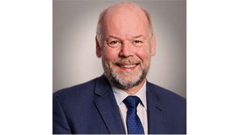 Male with grey hair and beard, wearing blue blazer and tie with light grey blouse