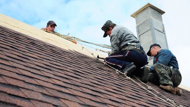 Roofers installing asphalt shingles on a rooftop with a chimney in Kyiv, Ukraine