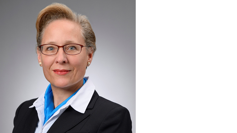 Female with short blonde hair wearing eye glasses, black suit, white blouse and blue neck scarf