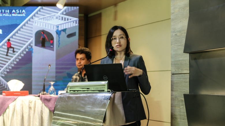 Female speaker on the podium wearing grey suit and eyeglasses