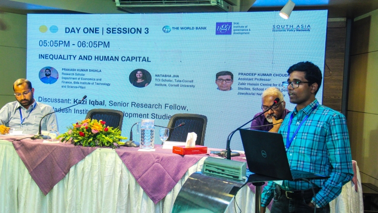 Male speaker on the podium wearing a striped turquoise blouse and eyeglasses