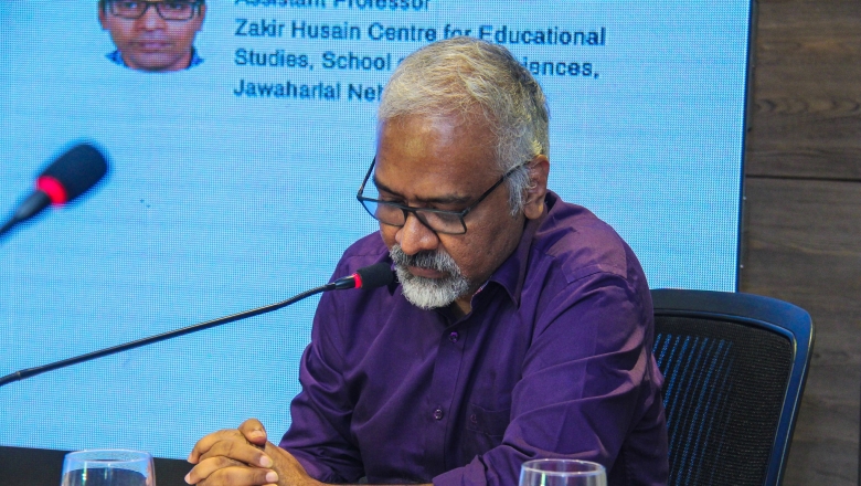 Male speaker on stage wearing purple blouse and eyeglasses 