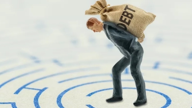 a plastic figure carrying a bag labeled debt on top of a 2d map