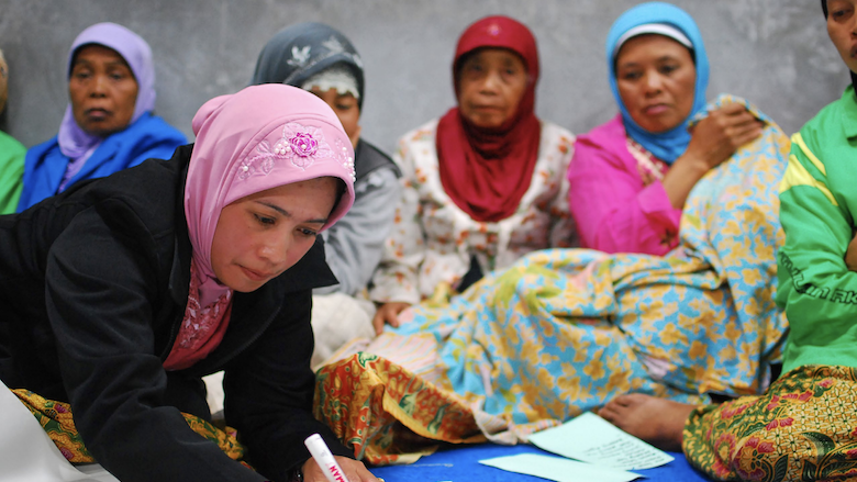 A woman is writing on the paper with a marker, and other women behind her are watching her writing. 