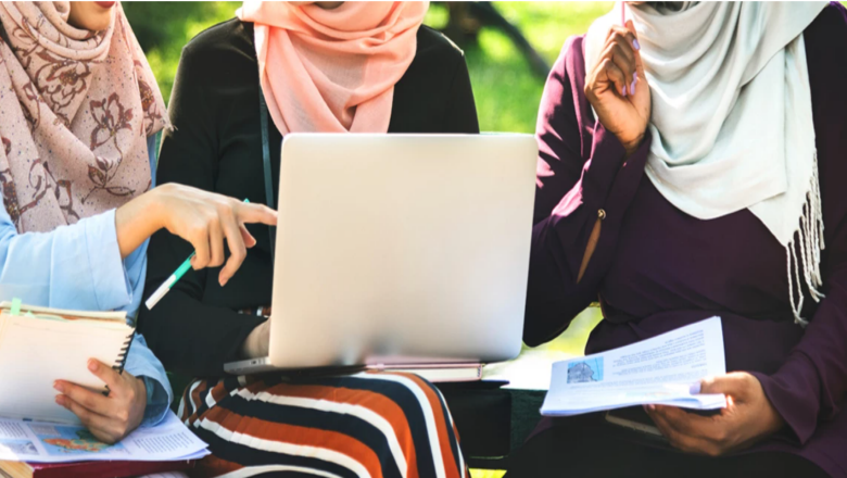 Women of different ethnicities chat and smile while working on their assignments and using a laptop to complete them