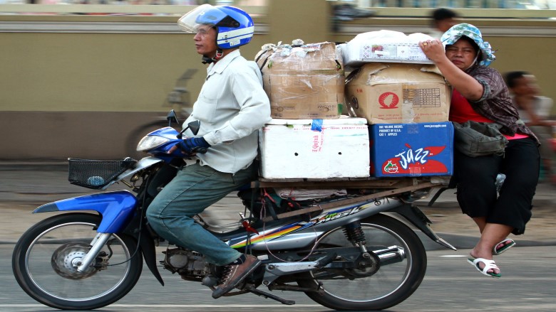 A bike loaded with goods, carrying two passengers, with one of them perched precariously on the bike.