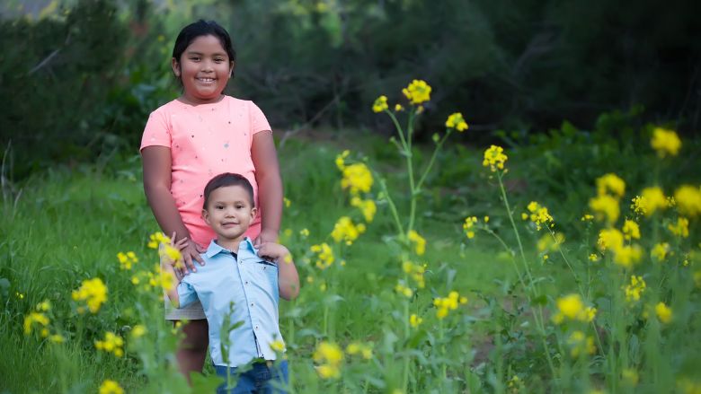 A young girl and boy from Ecuador smile while standing amid a green field