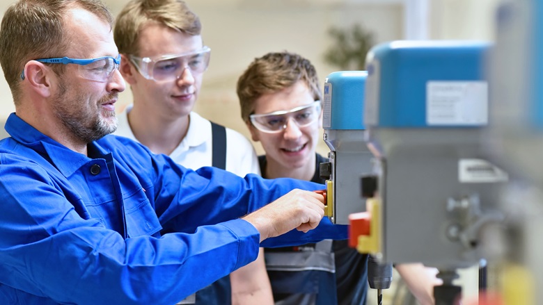 A vocational training teacher shows two young men how to operate a mechanical press