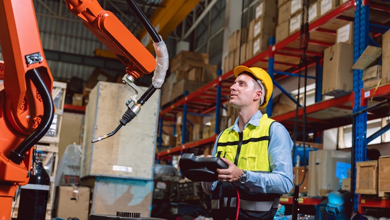 Engineer programming a robotic arm in a factory warehouse
