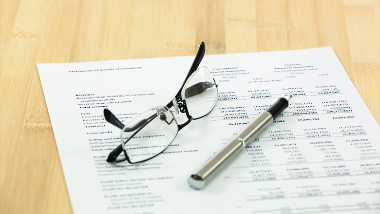 Close-up of documents, accompanied by reading glasses and a pen on a wooden desk