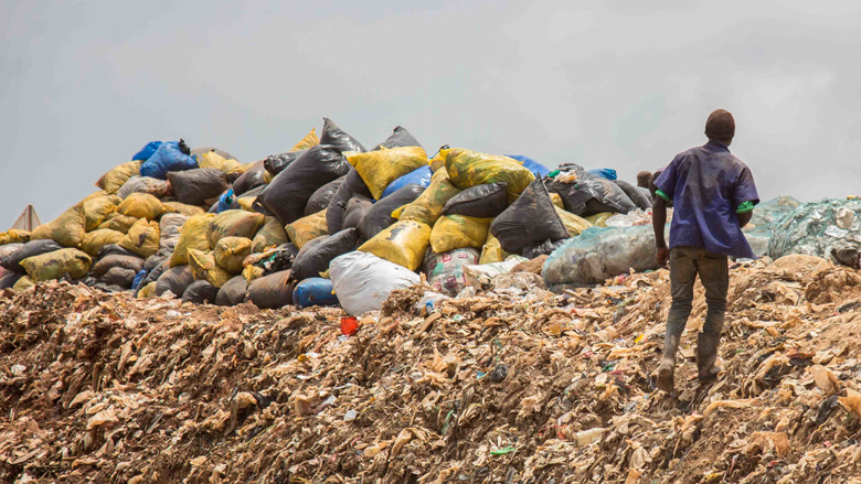 Person walking in a landfill, near a pile of plastic bags full of trash